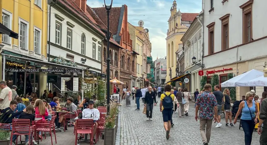 Tłum ludzi spaceruje brukowaną ulicą w Wilnie, siedząc przy stolikach restauracyjnych. Czy wyjazd na Litwę jest bezpieczny? Wygląda na to, że tak!