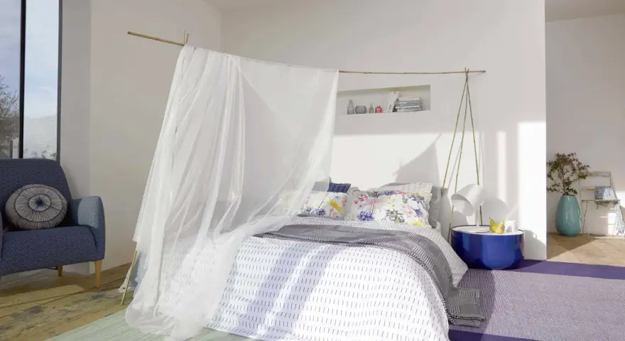 Acogedora habitación marinera con cama con dosel de tul, sillón azul y alfombras de colores.