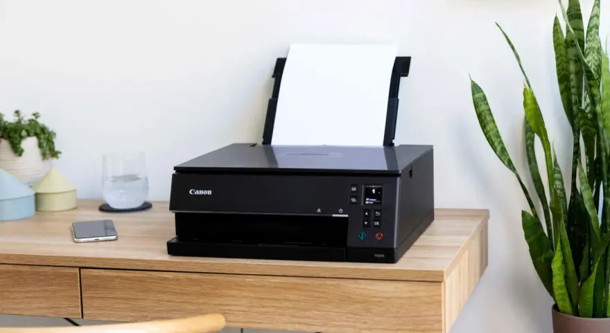 Schwarzer Canon Pixma Drucker mit WLAN verbinden. Ein Smartphone und ein Glas Wasser stehen daneben.