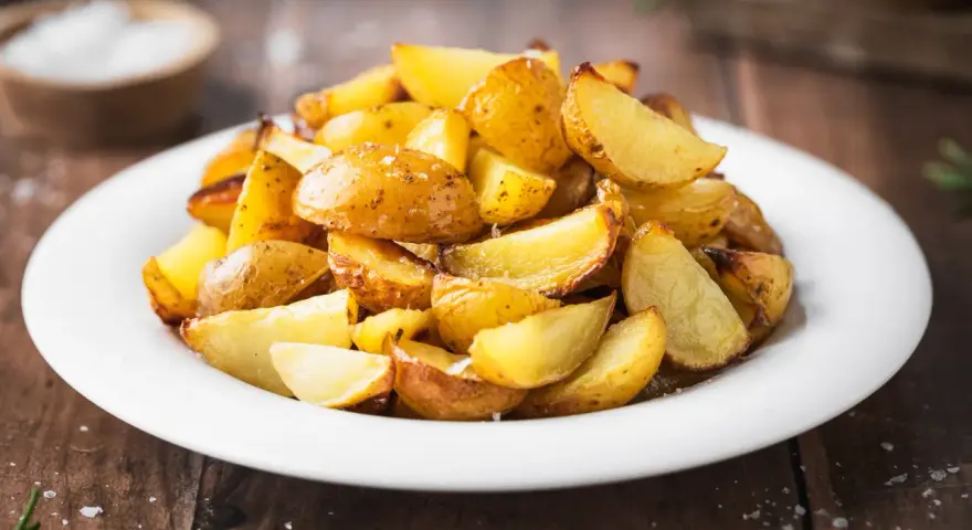 Patate al forno con buccia, dorate e croccanti, servite su un piatto bianco. Un contorno semplice e gustoso.