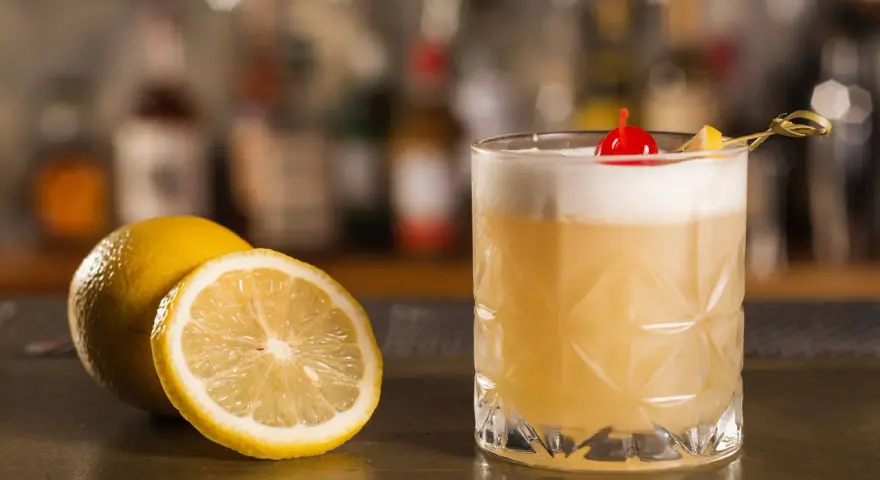 Orzeźwiający drink z amaretto, ozdobiony wiśnią i cytryną, stoi obok świeżych cytryn na barze.