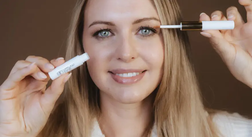 Frau mit blauen Augen trägt ein Serum auf ihre Wimpern auf, um sie wachsen zu lassen.