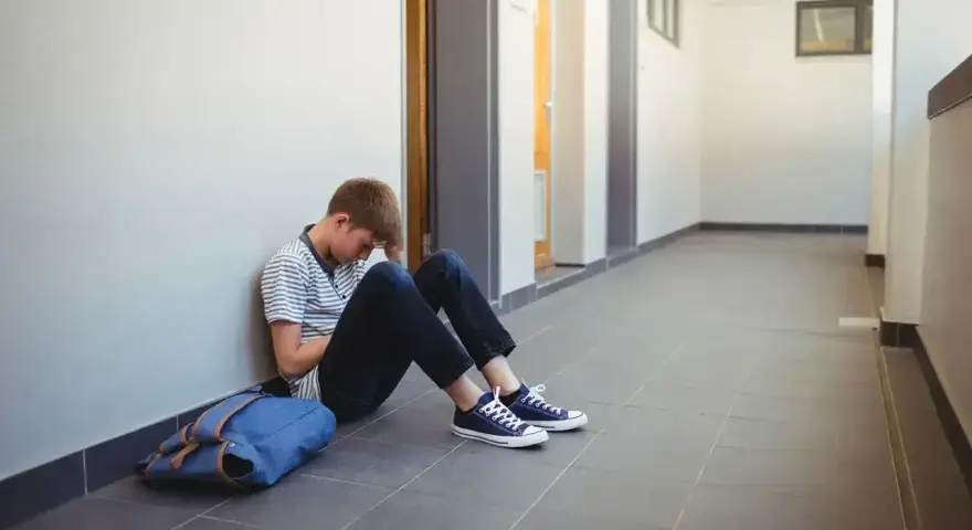 Chłopiec siedzi na korytarzu, przygnębiony. Może potrzebuje pomocy kuratorium?