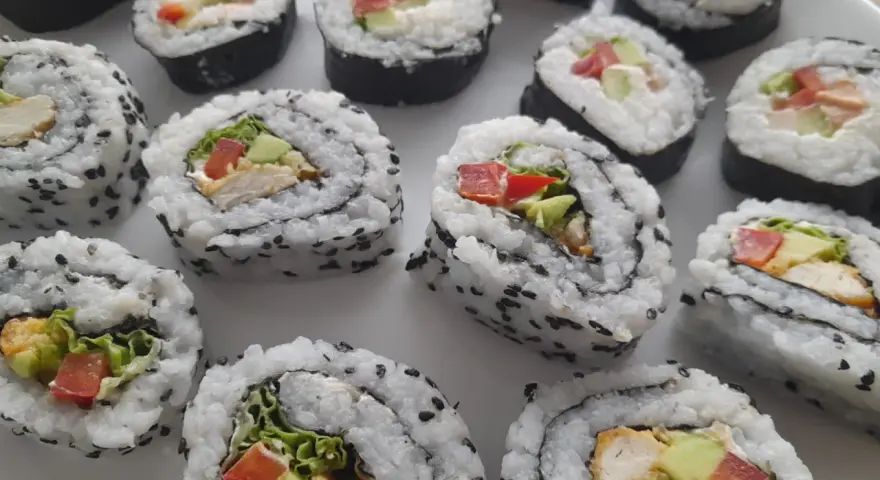 Pyszne domowe sushi z kurczakiem, awokado i warzywami, posypane czarnym sezamem.