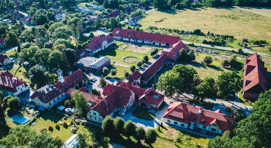 Widok z lotu ptaka na kompleks budynków hotelowych z czerwonymi dachami. Wiele pozytywnych kadyny folwark hotel & spa opinie potwierdza urok tego miejsca.