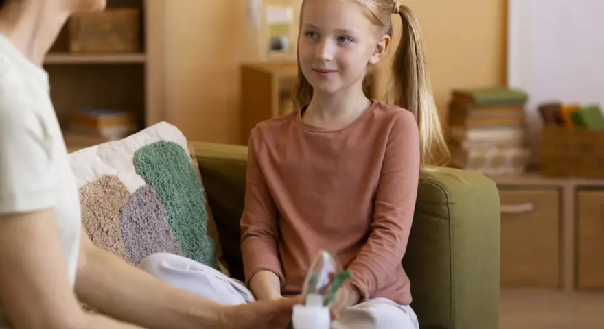 Rozmowa psychologa z rodzicem o zdrowiu dziecka. Dziewczynka z piegami słucha uważnie.