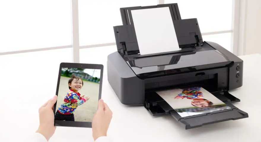 Jak włożyć papier fotograficzny do drukarki? Na tablecie zdjęcie dziecka, drukarka drukuje to samo zdjęcie.