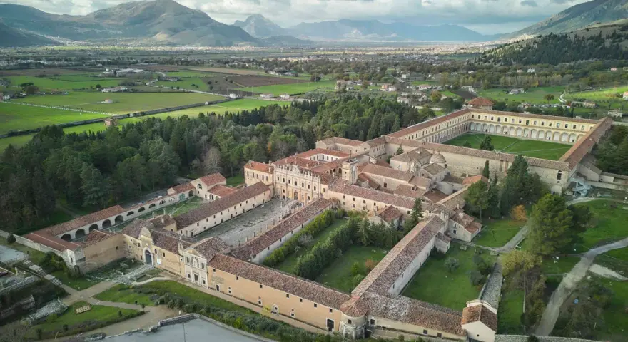 Vasta Certosa di Padula, un complesso monastico imponente con cortili verdi, circondato da alberi e montagne sullo sfondo.