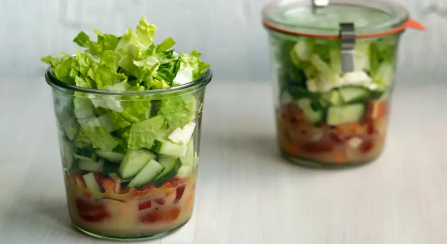 Frischer Salat im Glas, perfekt für eine Party. Schichten aus knackigem Salat, Gurken und Tomaten mit Dressing.