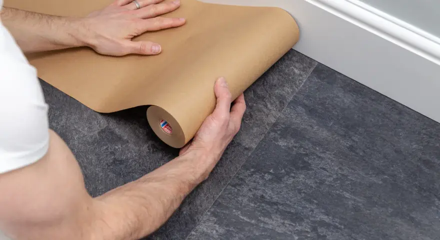 Ręce rozwijają brązowy papier, zabezpieczając podłogę podczas remontu.