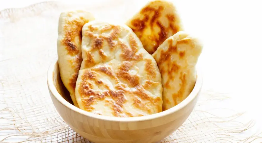 Kilka świeżo upieczonych chlebków naan w drewnianej misce.
