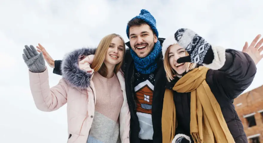 Drei Freunde genießen das Wandern im Winter. Sie tragen warme Kleidung wie Daunenjacken, Mützen und Handschuhe.