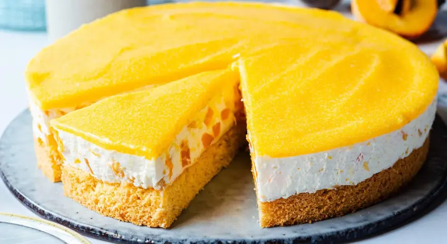 Eine saftige Pfirsich Maracuja Torte mit Biskuitboden, cremiger Füllung und fruchtigem Topping. Ein Stück ist bereits angeschnitten.