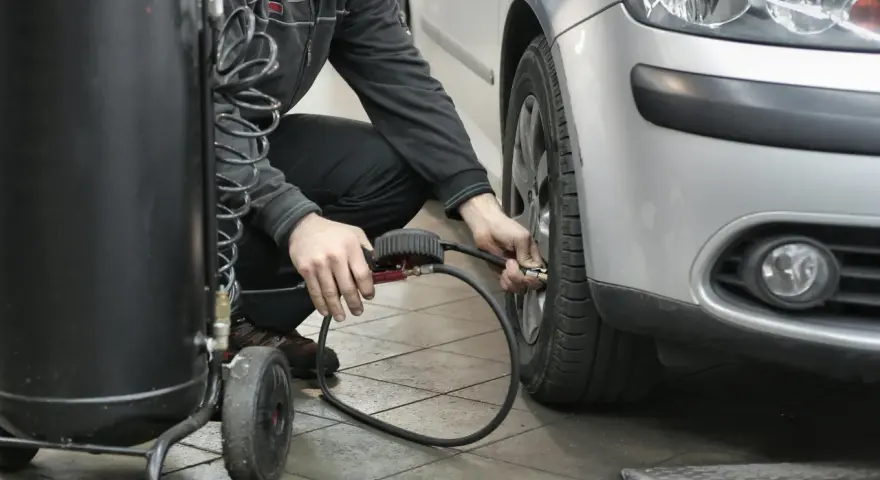 Un homme gonfle un pneu de voiture avec un manomètre et un compresseur.