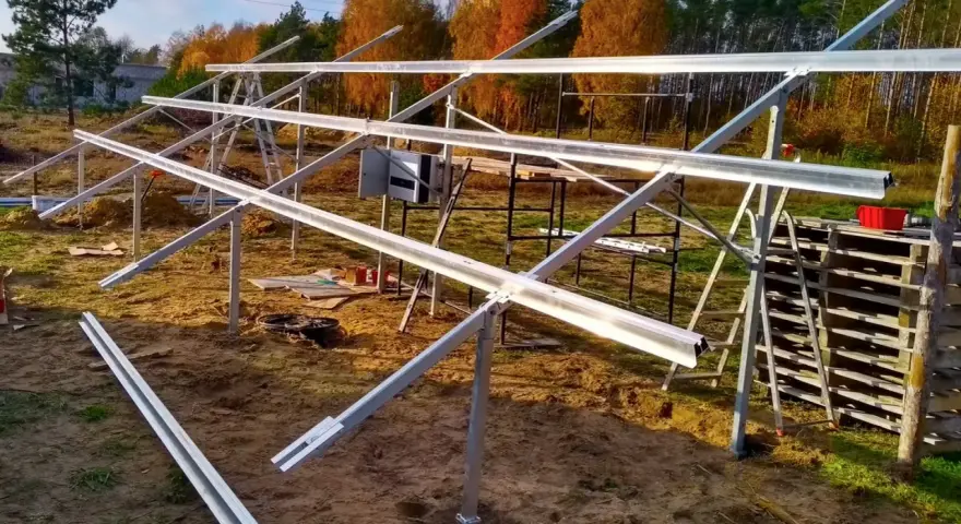 Metalowa konstrukcja pod panele fotowoltaiczne na gruncie, w trakcie montażu. W tle jesienne drzewa.