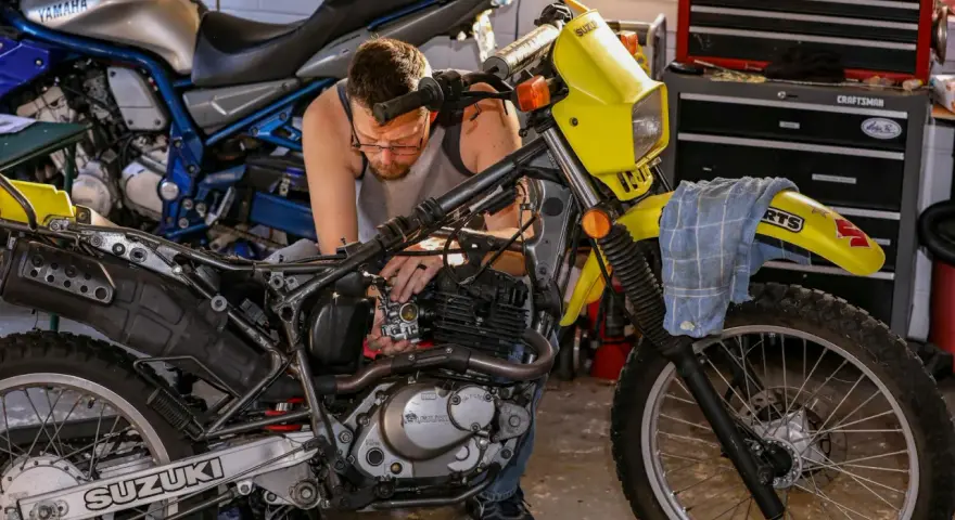 Mężczyzna majstruje przy żółtym motocyklu Suzuki. Rozrusznik kręci, a motocykl nie odpala.