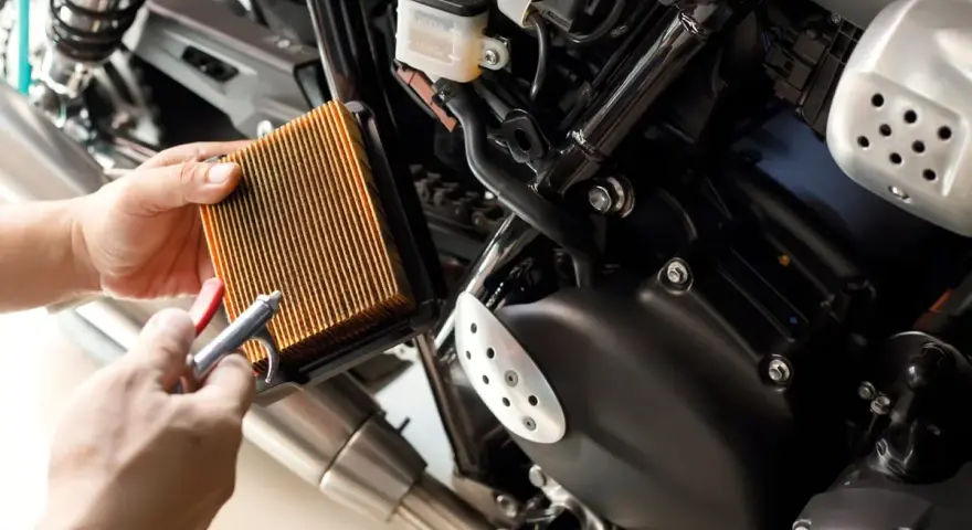 Mani puliscono il filtro dell'aria di una moto con aria compressa. Un filtro pulito è essenziale per il corretto funzionamento del motore, garantendo che a cosa serve il filtro dell'aria.
