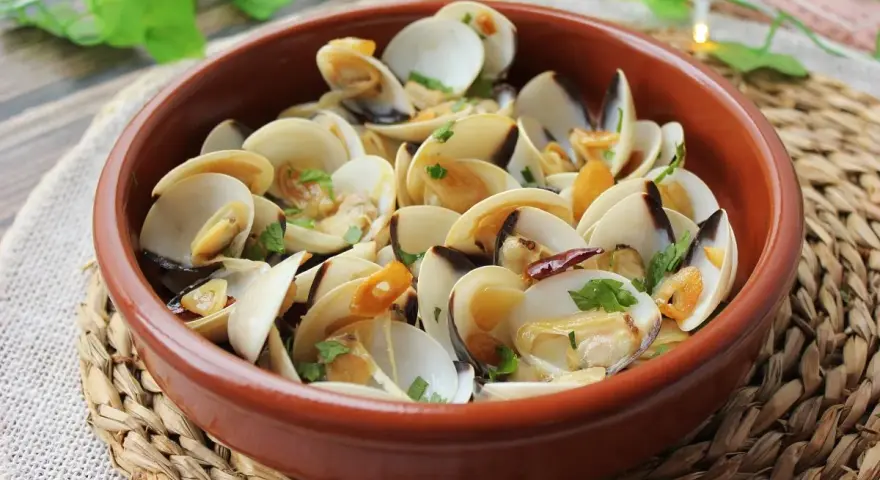 Deliciosas almejas al ajillo, servidas en una cazuela de barro, con ajo laminado y perejil fresco.