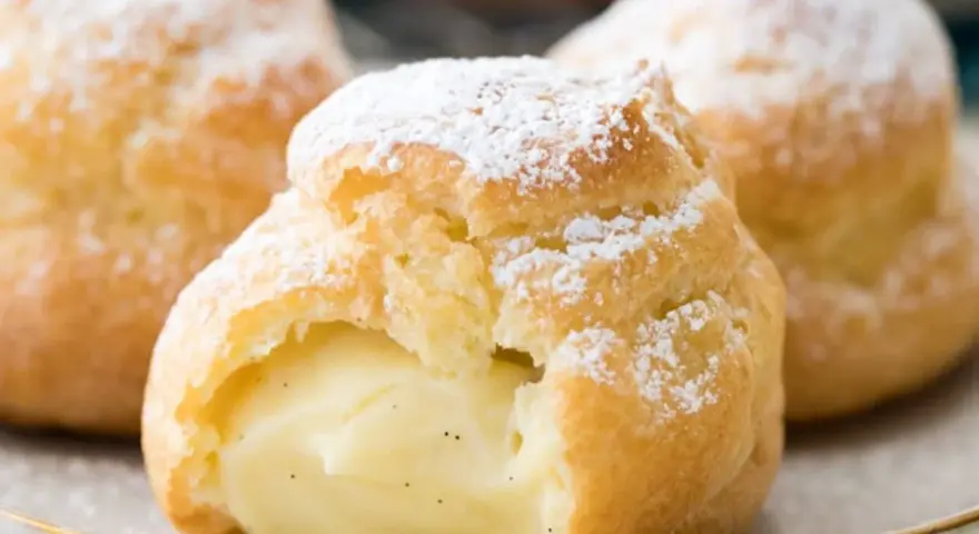 Trois choux à la crème généreusement garnis de crème pâtissière à la vanille, saupoudrés de sucre glace.