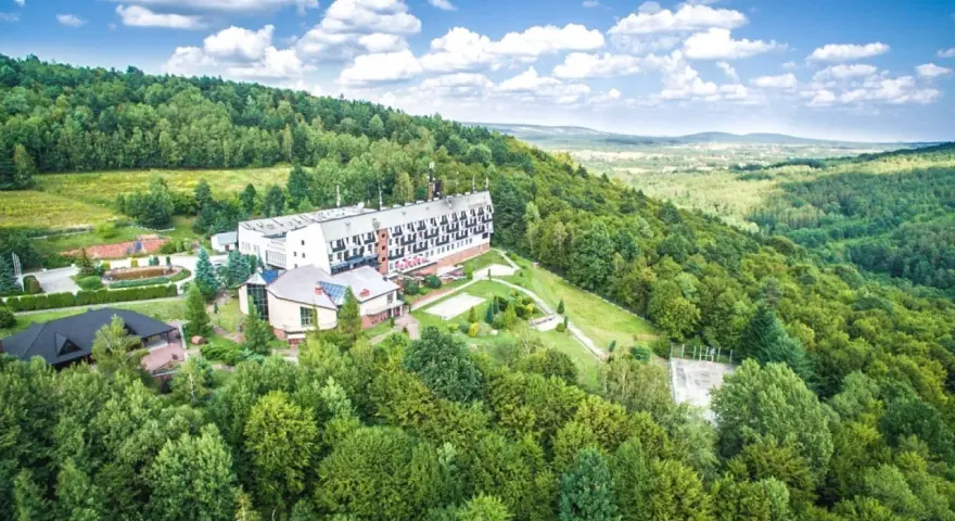 Hotel w otoczeniu zielonych lasów Gór Świętokrzyskich, blisko Kielc. Widok z lotu ptaka na budynki i krajobraz.