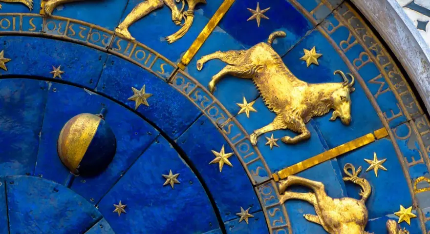 Złoty koziorożec na niebieskiej tarczy zegara astronomicznego, otoczony gwiazdami i cyframi. Dlaczego koziorożec milczy? Może czeka na swój czas.
