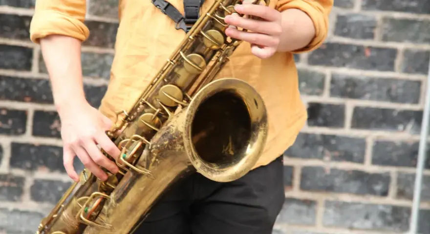 Hände spielen ein goldenes Saxophon. Obwohl es aus Metall ist, ist das Saxophon ein Holzblasinstrument, da der Ton durch ein Rohrblatt erzeugt wird.