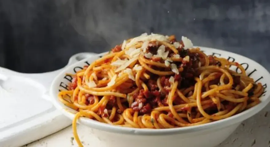 Gorące spaghetti z sosem bolońskim i parmezanem, parujące w misce. Czy to bucatini czy spaghetti, smakuje wyśmienicie!