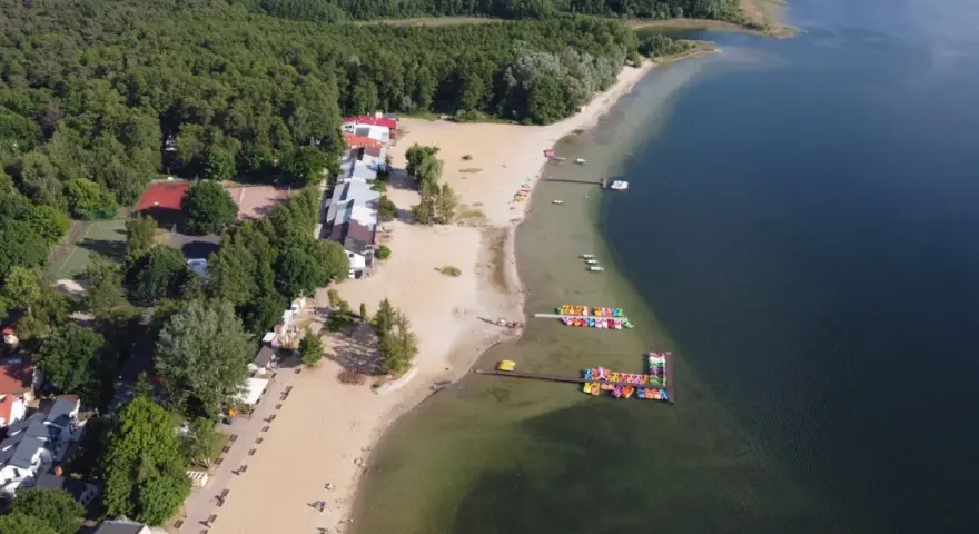 Skorzęcin jezioro z lotu ptaka: piaszczysta plaża, kolorowe rowery wodne, budynki i las.