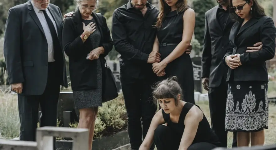 Famiglia in lutto, vestiti di nero, si riunisce al cimitero. Un esempio di come vestirsi a un funerale, con abiti sobri e rispettosi.