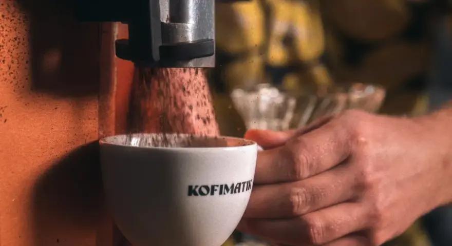 Mielona kawa spada do filiżanki z napisem "Kofimatik". Idealna baza do kawy z likierem kawowym Baileys.