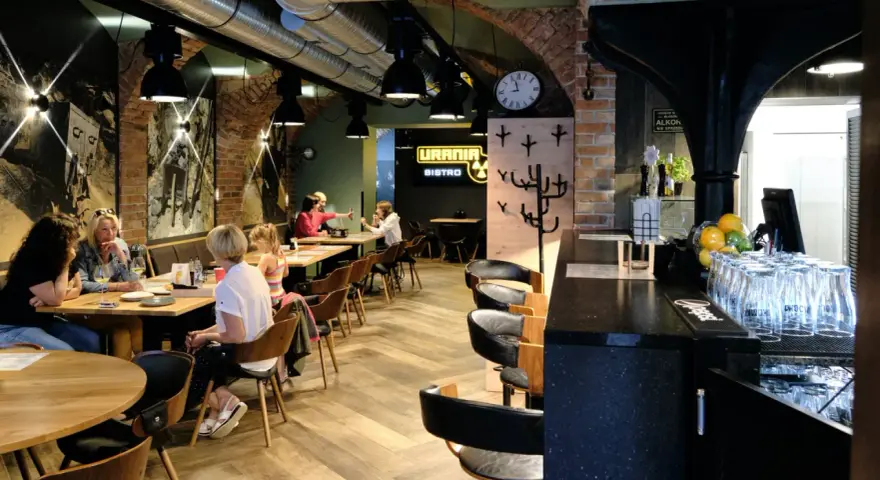 Wnętrze restauracji Urania Bistro z ludźmi przy stołach i barem.