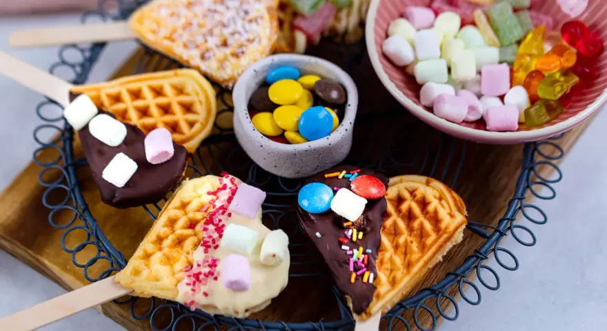 Herzförmige Waffeln am Stiel, dekoriert mit Schokolade, Marshmallows und Streuseln. Ein süßes Rezept für Waffeln am Stiel!