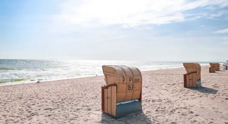 Strandkörbe am Dahme Strand unter blauem Himmel. Das Meer glitzert in der Sonne.