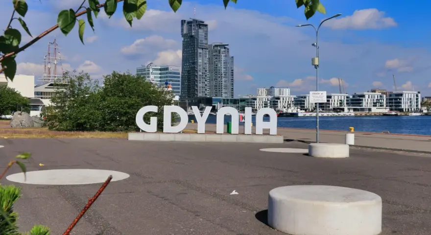 Napis GDYNIA na tle nowoczesnej architektury i żaglowca. Widok na port i budynki w Gdynia old town.