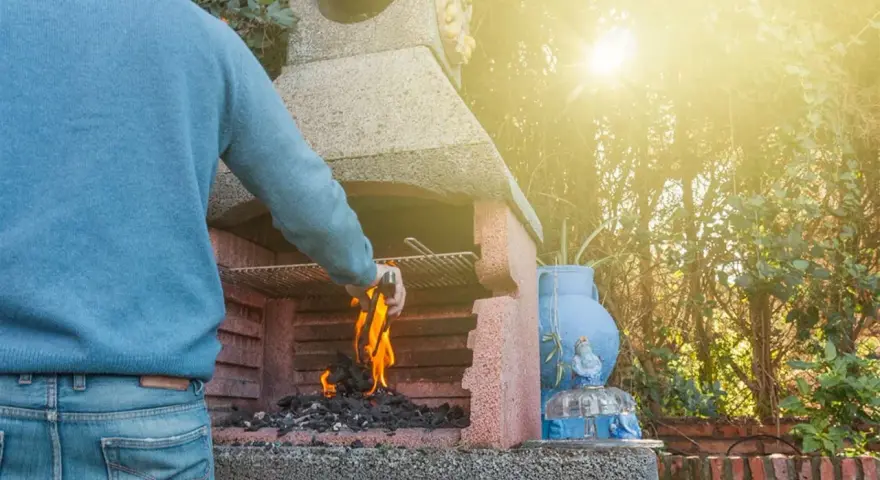 Hombre aviva las brasas en una de las **tipos de barbacoas de obra**, lista para una parrillada.