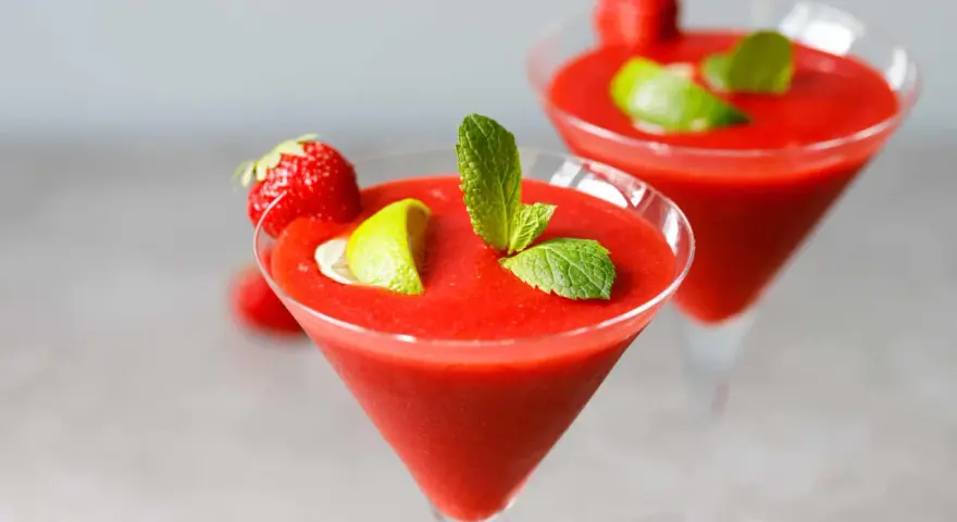 Dwa mrożone strawberry daiquiri, ozdobione truskawkami, limonką i miętą, gotowe do orzeźwiającej degustacji.
