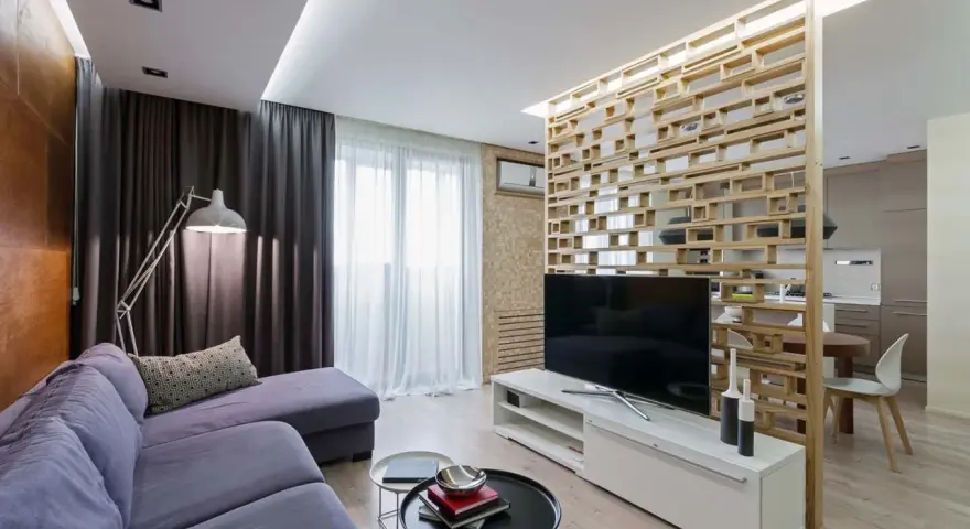 Acogedor salón de 18 metros cuadrados con sofá morado, lámpara de pie y separador de ambiente de madera.