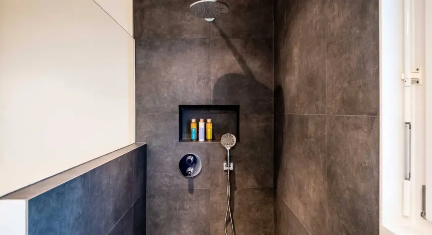 Ducha moderna con tabique de obra y muro de cristal. Incluye alcachofa de lluvia, grifería empotrada y nicho con botes de champú.