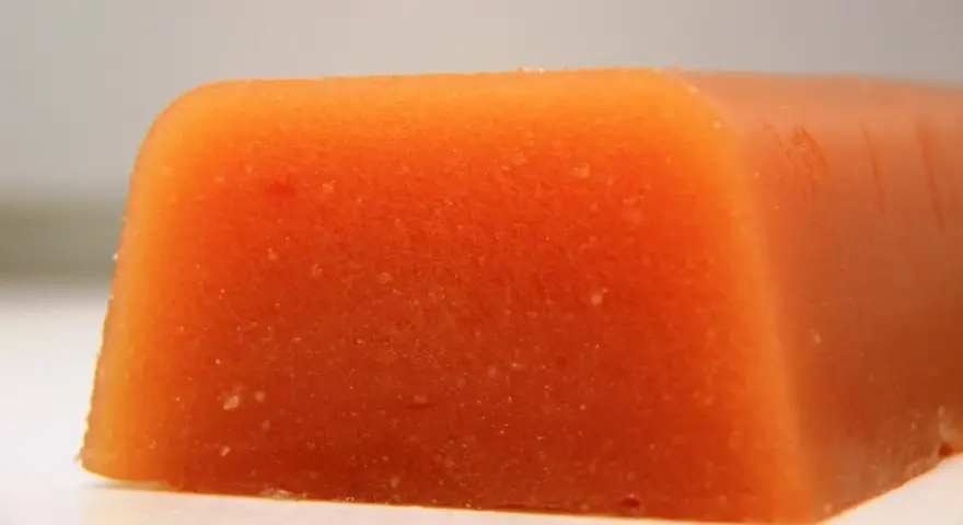 Bloque naranja de carne de membrillo, con textura granulada y bordes redondeados.
