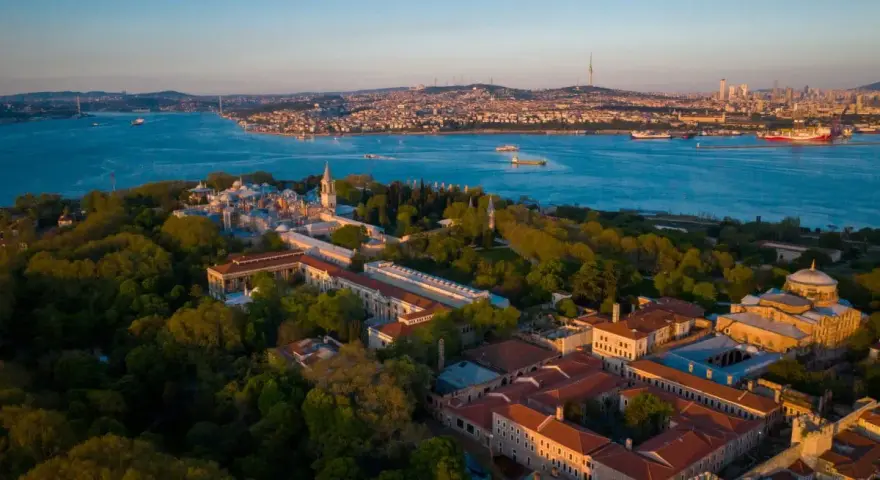 Aerial view of the Topkapi Palast complex, nestled amongst lush greenery, with the Bosphorus Strait and Istanbul skyline in the background.
