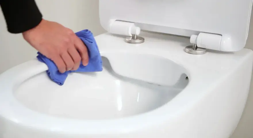 Main propre avec un chiffon bleu, nettoyant le bord d'un wc avec bride ou sans bride.