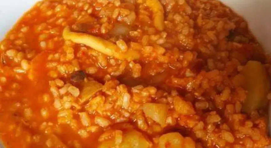 Arroz caldoso con trozos de marisco y verduras en salsa rojiza.