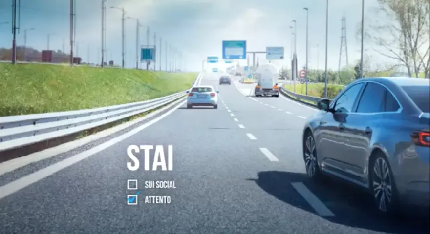 Sulla strada, auto e camion procedono. "STAI ATTENTO" è scritto, ricordando l'art. 79 CDS.