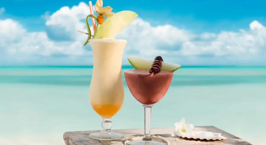 Dwa egzotyczne drinki, jeden kremowy, drugi owocowy, z Malibu na tropikalnej plaży. Idealne na wakacje.