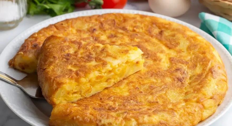 Złocista tortilla ziemniaczana, idealna na szybki obiad z niczego. Na talerzu, obok pomidorów i jajek.