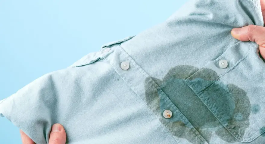 Main d'une personne tenant une chemise bleu pâle avec une grande tache d'huile sur le devant, prête à enlever une tache d'huile avec du bicarbonate.