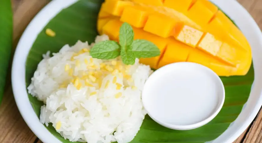 Pyszny mango sticky rice: ryż kleisty z kawałkami mango, polany mleczkiem kokosowym, udekorowany miętą.