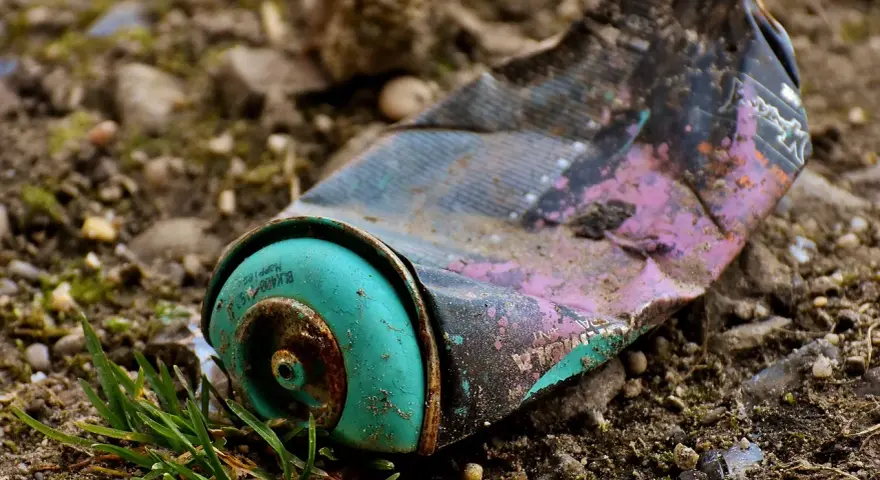 Lata de aerosol aplastada y oxidada en el suelo, un ejemplo de las causas de la contaminación.