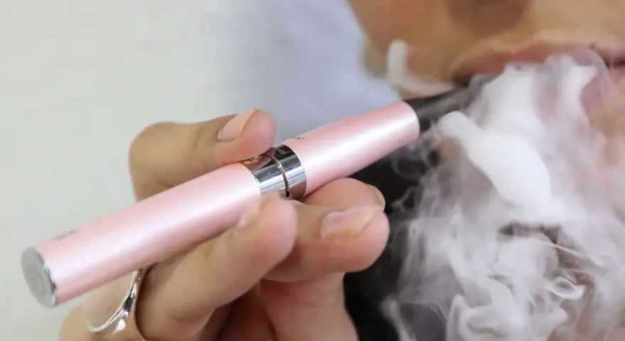 Persona exhala vapor de un cigarrillo electrónico rosa. ¿Qué es peor el vaper o el tabaco?