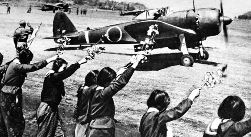 Des jeunes Japonais agitent des fleurs vers un avion, peut-être un adieu avant une mission kamikaze.